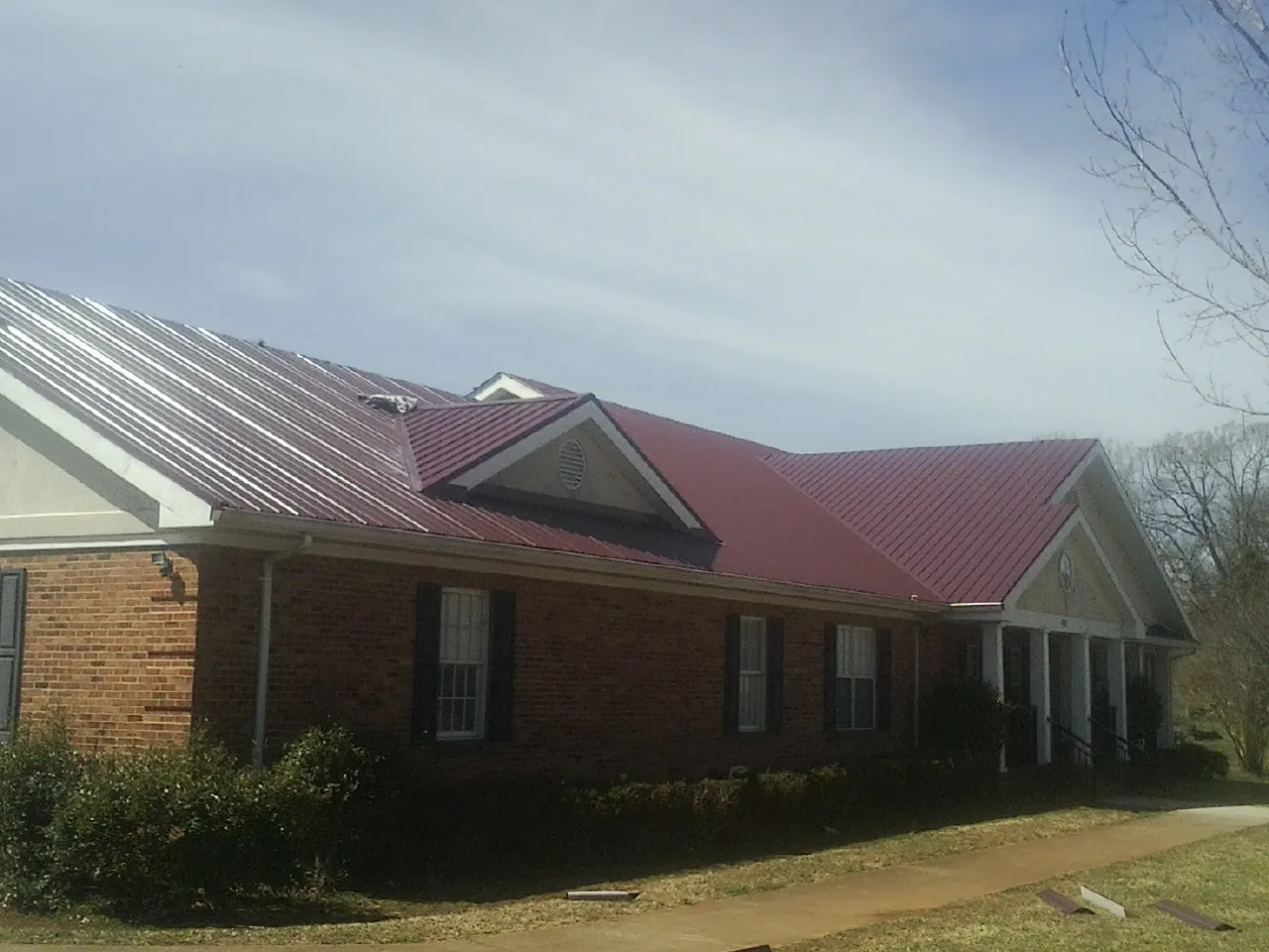 Red metal roof with gabled entries on a long brick building, from a Hail Damage Roof Repair job in Weaverville