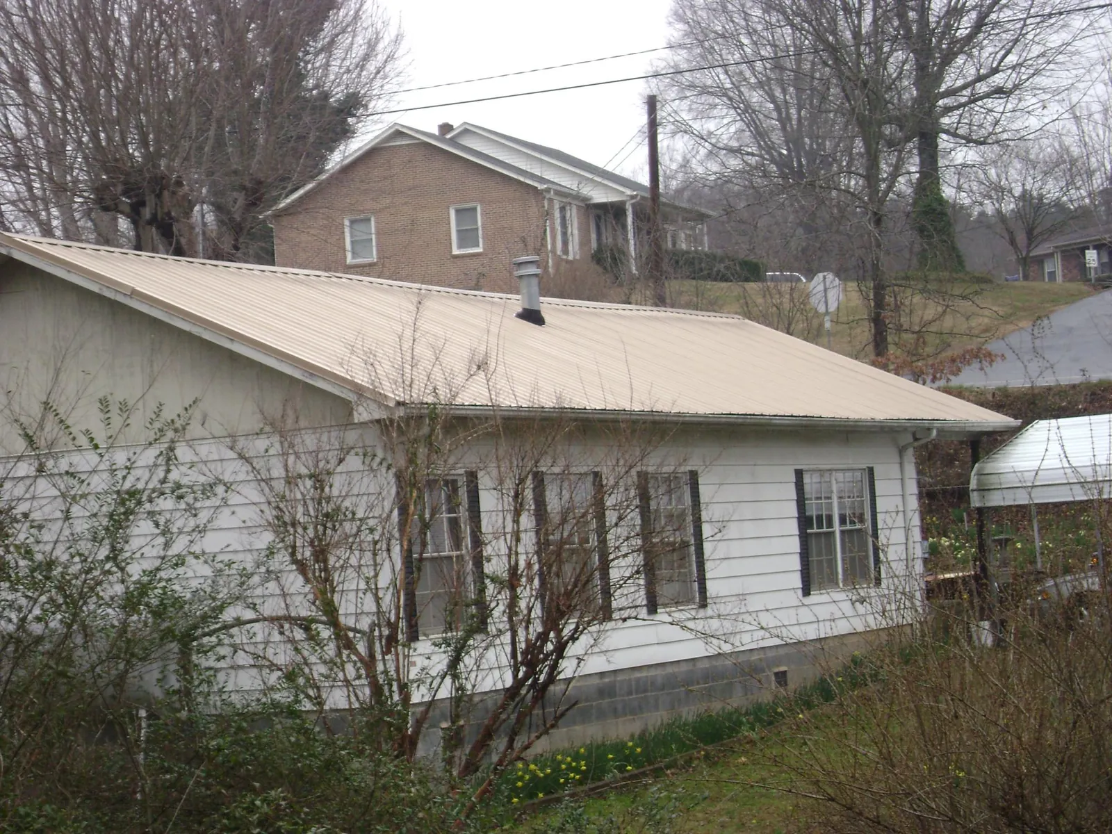 Tan metal roof on a white sided house set into a hillside — Commercial Roofing by Roofing Brothers in Weaverville
