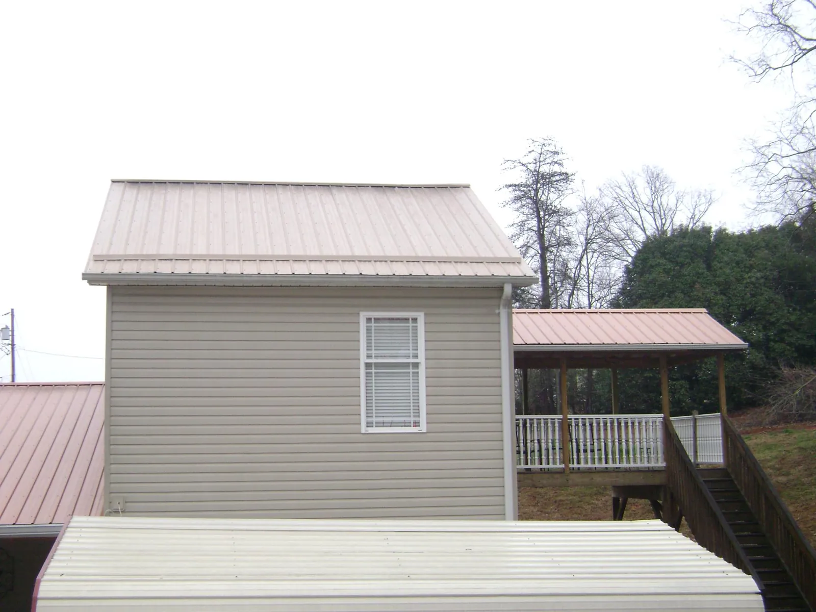 Tan metal roofs on a two story addition and attached porch, from a Roof Replacement job in Weaverville
